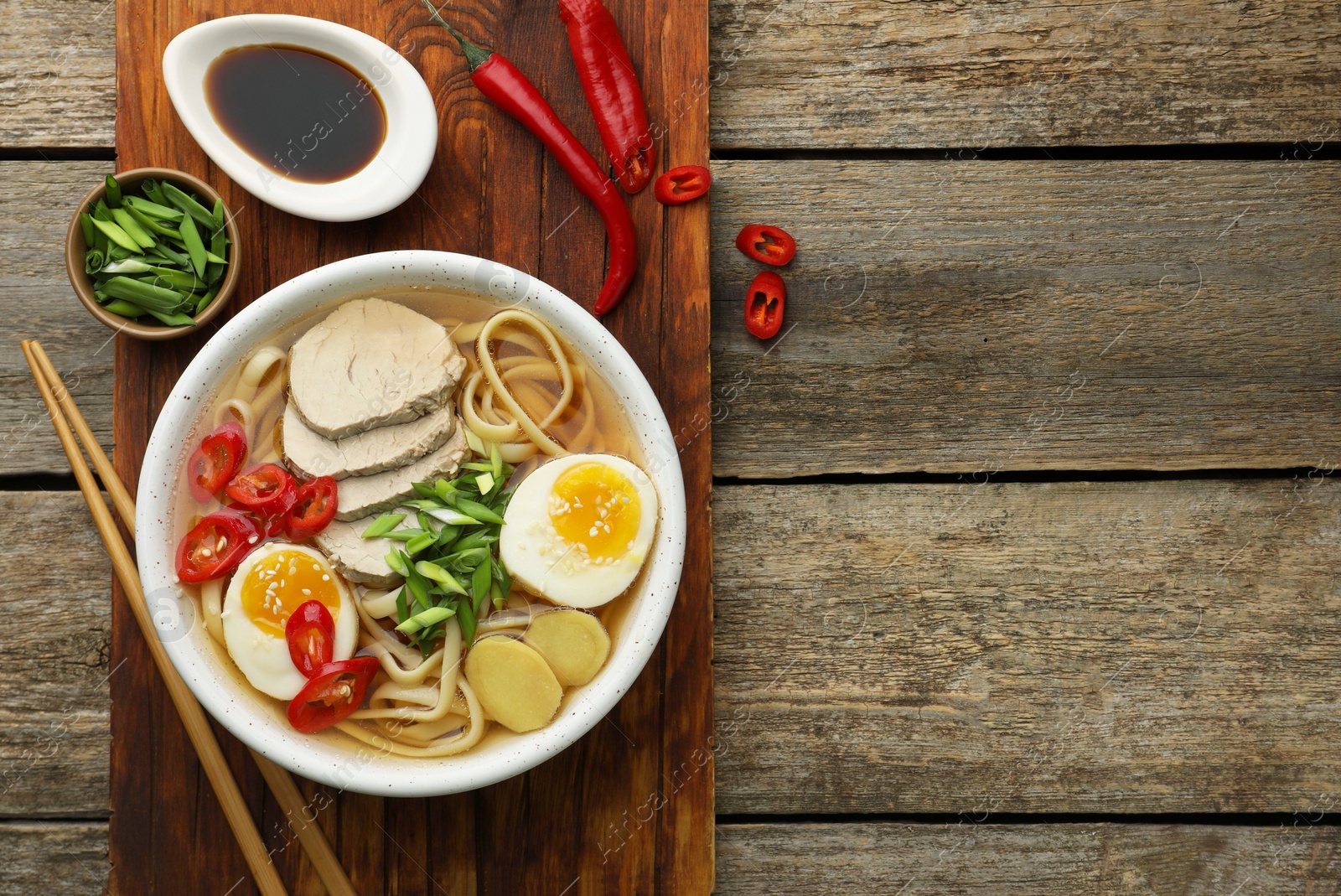 Photo of Delicious ramen in bowl served on wooden table, flat lay and space for text. Noodle soup