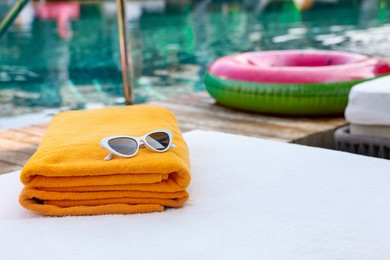 Beach towels and sunglasses on sun lounger near outdoor swimming pool, space for text. Luxury resort