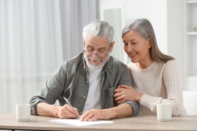 Photo of Senior couple signing Last Will and Testament indoors