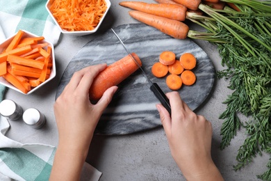 Woman cutting carrot at grey table, top view