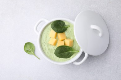 Delicious spinach cream soup with cheese in bowl on light grey table, top view