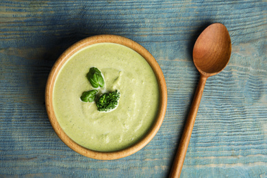 Photo of Delicious broccoli cream soup served on blue wooden table, flat lay