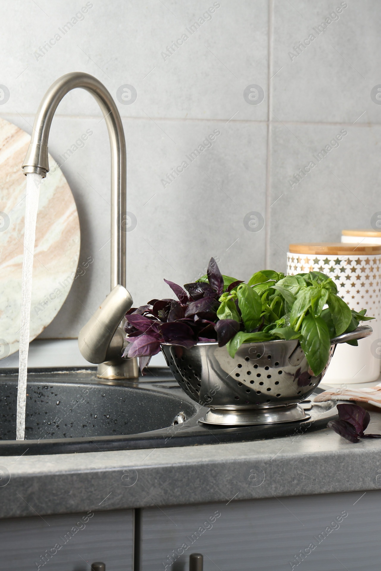 Photo of Metal colander with different fresh basil leaves on grey countertop near sink