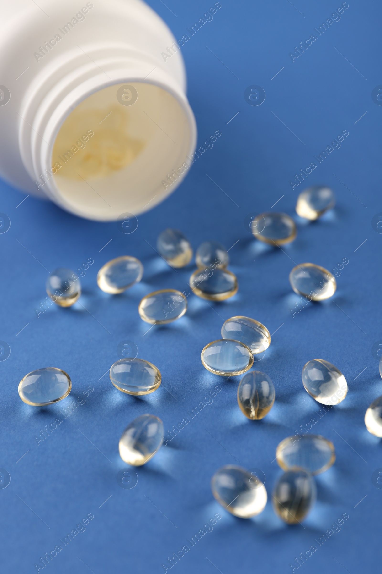 Photo of Bottle and vitamin capsules on blue background, closeup