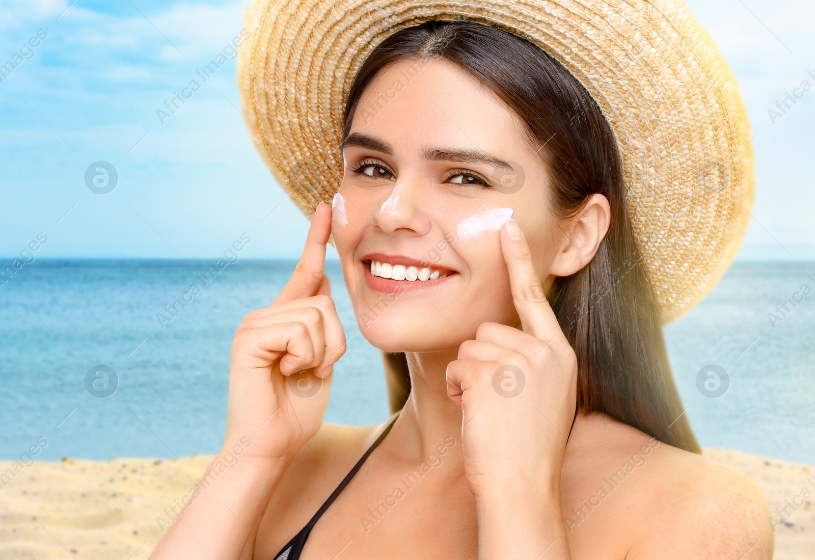 Image of Sun protection. Beautiful young woman applying sunblock onto face on beach, closeup