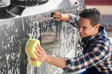 Photo of Worker cleaning automobile with sponge at car wash