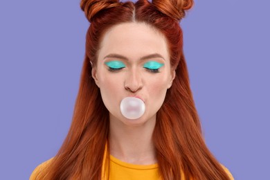 Photo of Beautiful woman with bright makeup and closed eyes blowing bubble gum on violet background