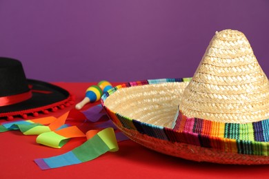 Mexican sombrero and black Flamenco hats on red table, closeup