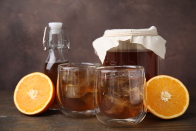 Photo of Tasty kombucha with ice cubes and orange on wooden table