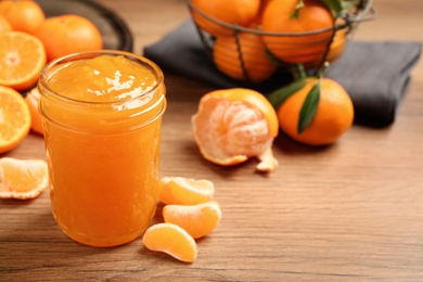 Photo of Delicious tangerine jam on wooden table. Space for text
