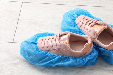 Photo of Women`s sneakers in blue shoe covers on light wooden floor