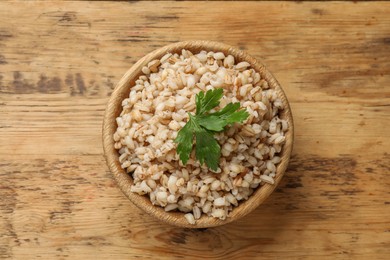 Photo of Delicious pearl barley with parsley in bowl on wooden table, top view