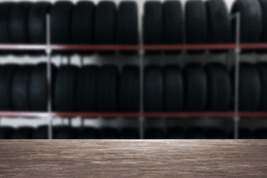 Empty wooden surface and blurred view of car tires in auto store, closeup. Space for text 