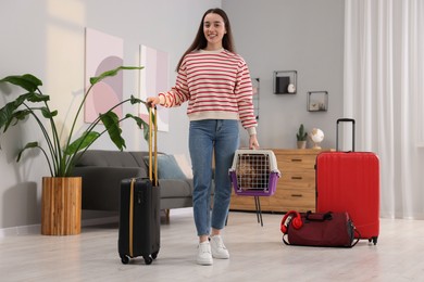 Photo of Travel with pet. Smiling woman holding carrier with dog and suitcase at home