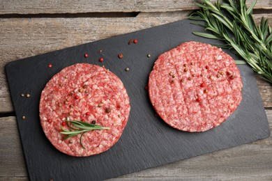 Raw hamburger patties with rosemary and peppercorns on wooden table, flat lay