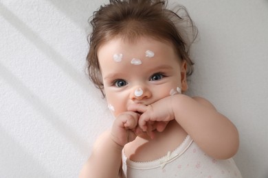 Photo of Cute little baby with cream on face in comfortable crib, top view. Space for text