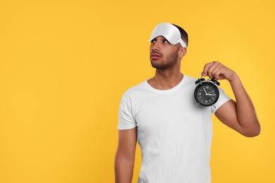 Photo of Tired man with sleep mask and alarm clock on orange background, space for text. Insomnia problem