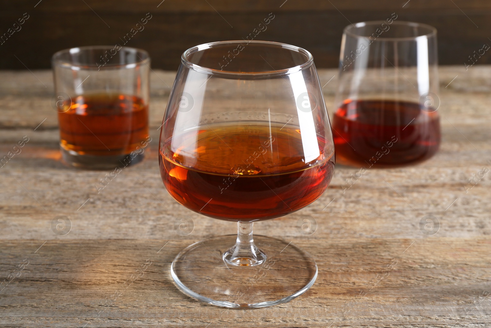 Photo of Different delicious liqueurs in glasses on wooden table