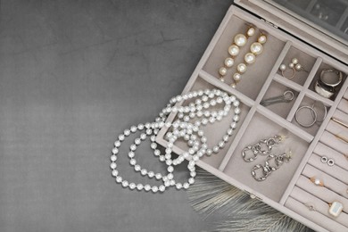 Photo of Jewelry box with many different accessories on grey table, top view. Space for text