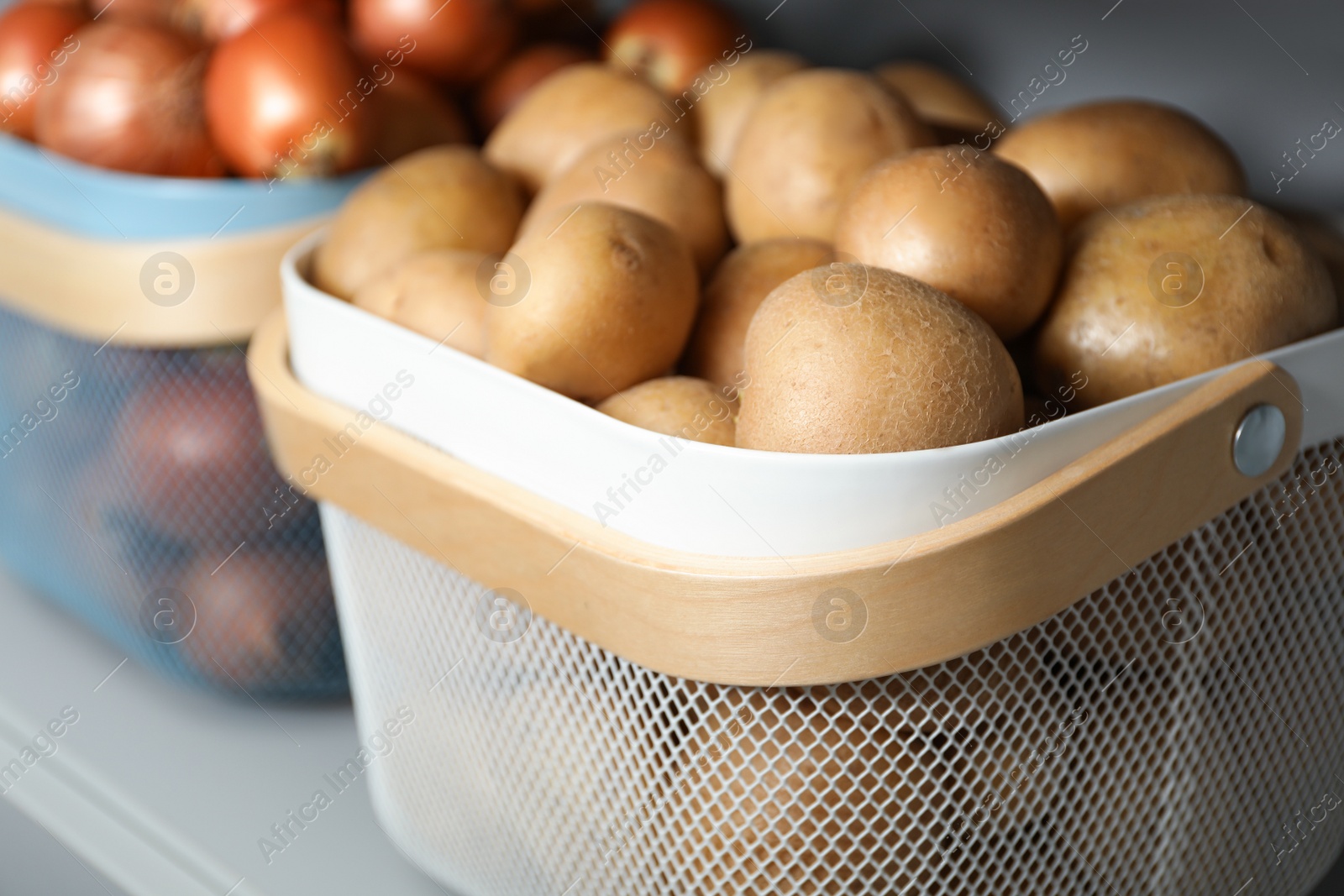 Photo of Baskets with potatoes and onions on shelf, closeup. Orderly storage