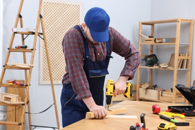 Young worker using electric drill at table in workshop