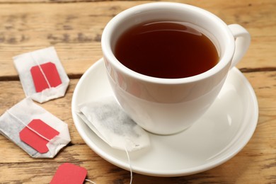 Photo of Tea bags and cup of hot beverage on wooden table, closeup