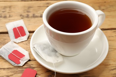 Tea bags and cup of hot beverage on wooden table, closeup