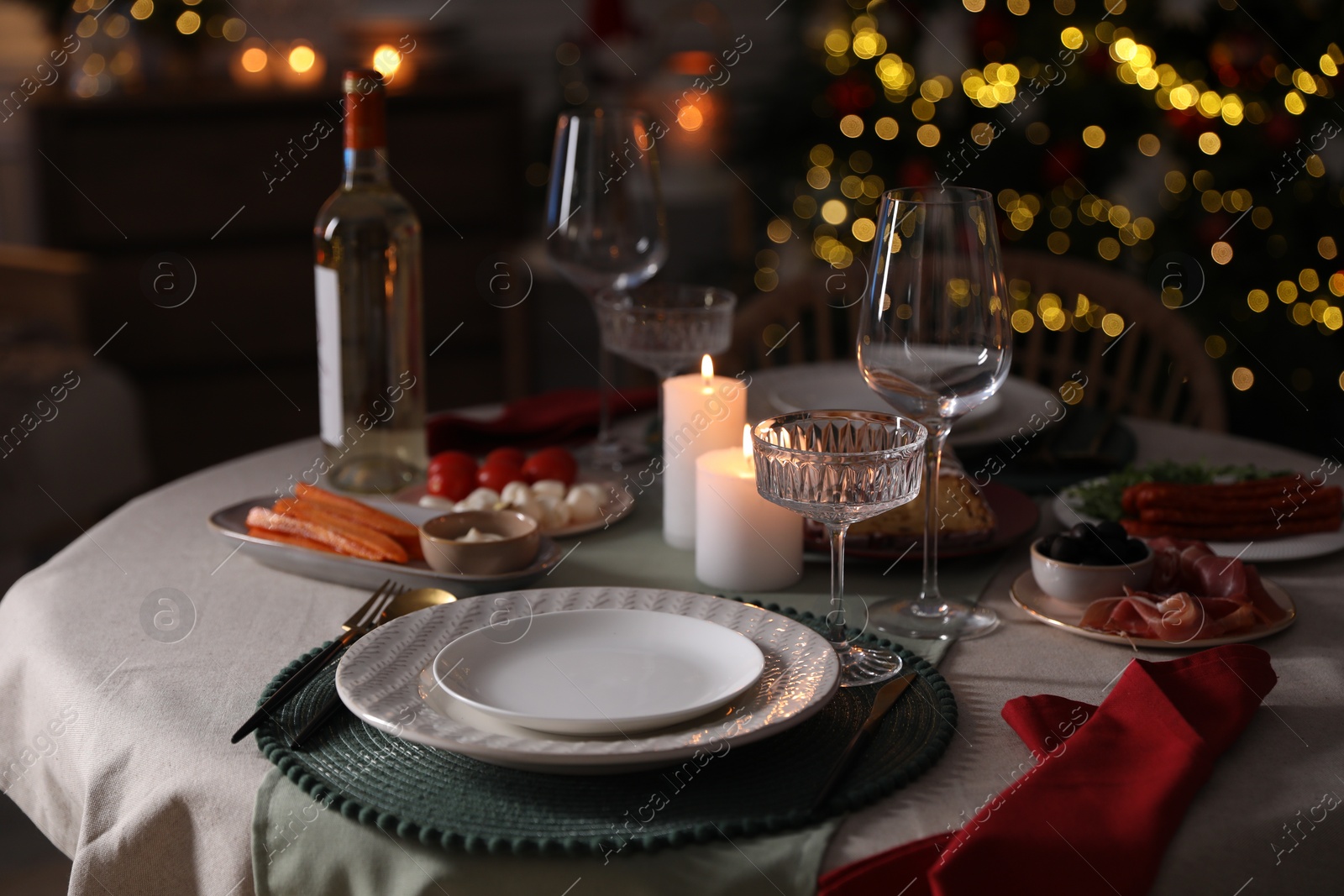 Photo of Christmas table setting with burning candles, appetizers and dishware indoors