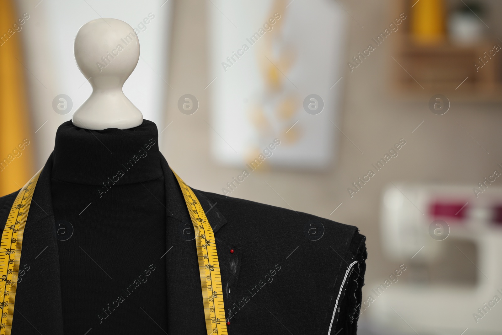 Photo of Mannequin with unfinished suit jacket and measuring tape in tailor shop, closeup. Space for text