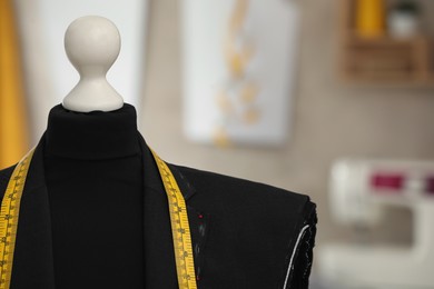 Photo of Mannequin with unfinished suit jacket and measuring tape in tailor shop, closeup. Space for text