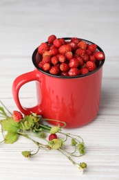 Fresh wild strawberries in mug and green stems on white wooden table