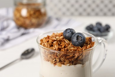 Tasty yogurt with muesli and blueberries in cup served on white table, closeup