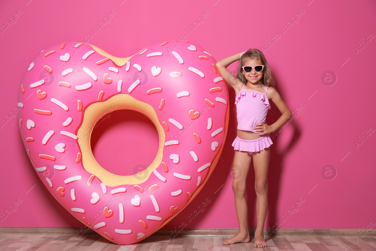 Photo of Cute little girl with bright heart shaped inflatable ring near color wall