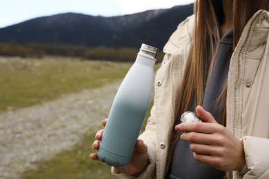 Photo of Woman holding thermo bottle and cap in mountains, closeup. Space for text