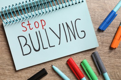 Photo of Text Stop Bullying written in notebook and markers on wooden table, flat lay