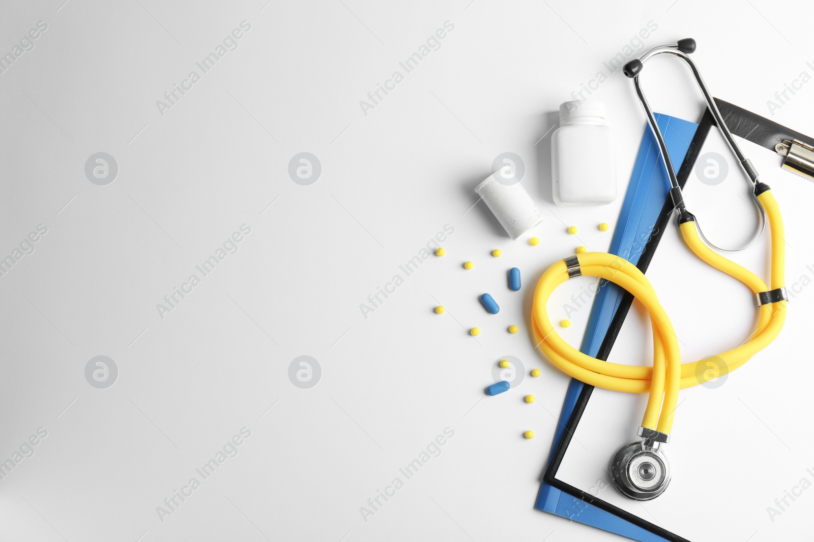 Photo of Stethoscope, clipboard and pills on light background, top view. Medical equipment