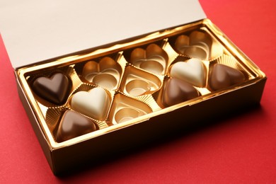Photo of Partially empty box of chocolate candies on red background, closeup