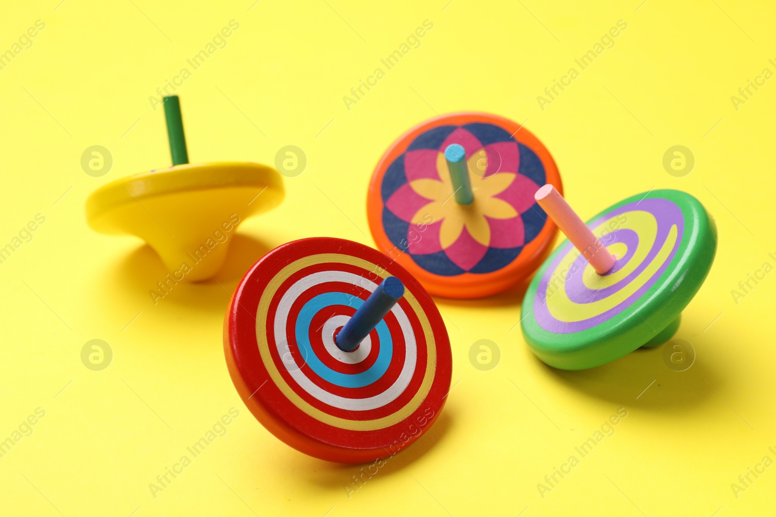 Photo of Many colorful spinning tops on yellow background, closeup