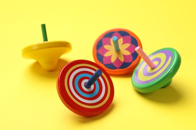 Photo of Many colorful spinning tops on yellow background, closeup