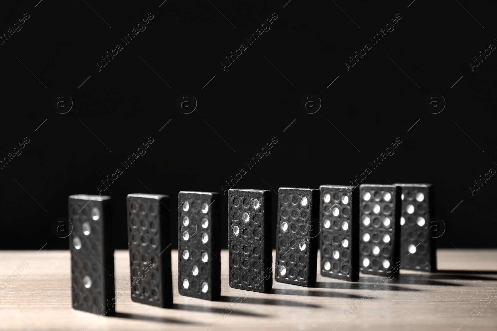 Photo of Domino tiles on wooden table against black background. Space for text