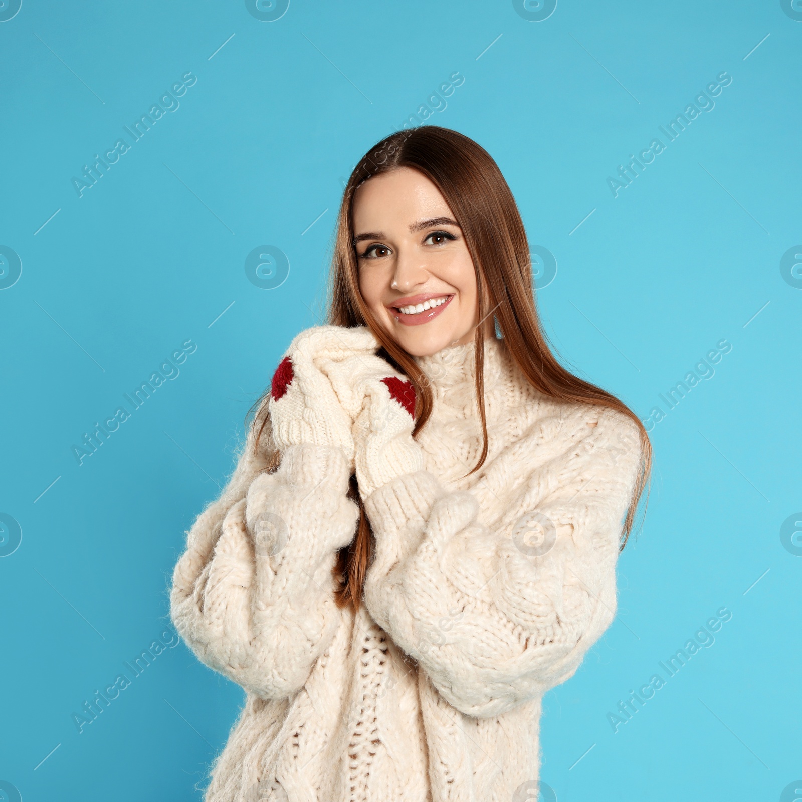 Photo of Beautiful young woman in mittens and white sweater on blue background. Winter season