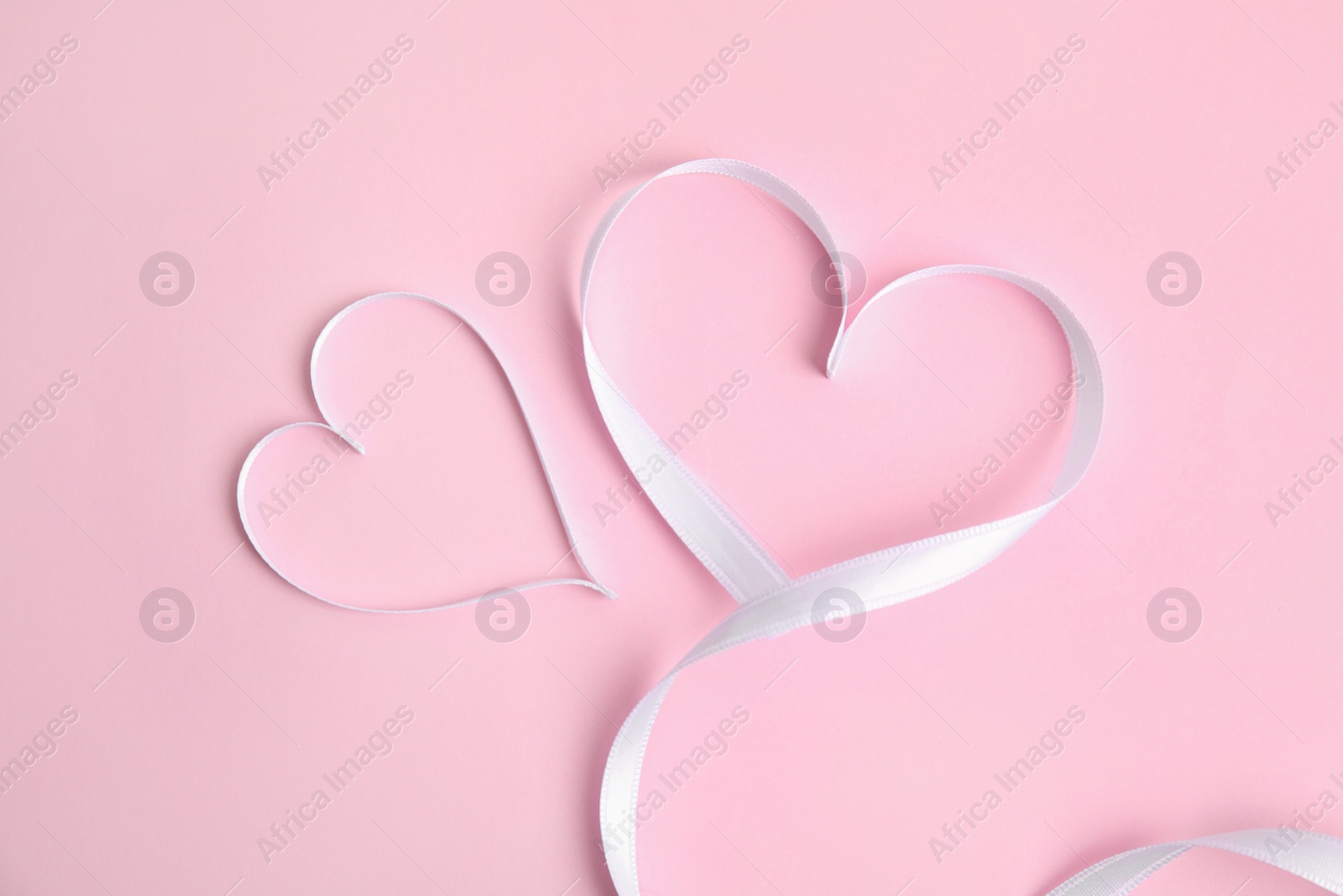 Photo of Hearts made of white ribbon on pink background, flat lay. Valentine's day celebration