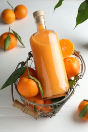 Photo of Bottle of tasty tangerine liqueur and fresh fruits in basket on white table
