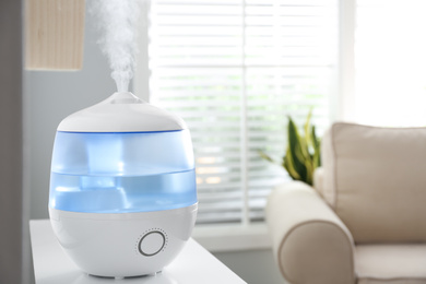 Photo of Modern air humidifier on table at home. Space for text