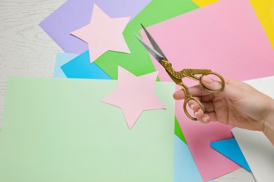 Photo of Woman holding beautiful scissors near colorful paper sheets at white wooden table, closeup. Space for text
