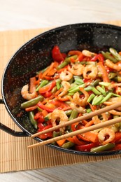 Shrimp stir fry with vegetables in wok on wooden table, closeup