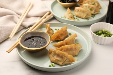 Photo of Delicious gyoza (asian dumplings) with soy sauce, green onions and chopsticks on white table