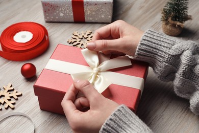 Photo of Christmas present. Woman tying ribbon bow on gift box at wooden table, closeup