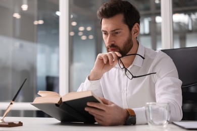 Photo of Handsome man reading book at table in office. Lawyer, businessman, accountant or manager