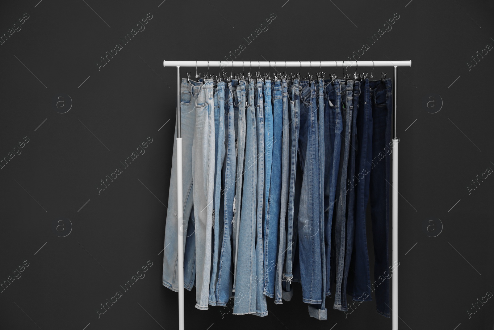 Photo of Rack with different jeans on dark grey background